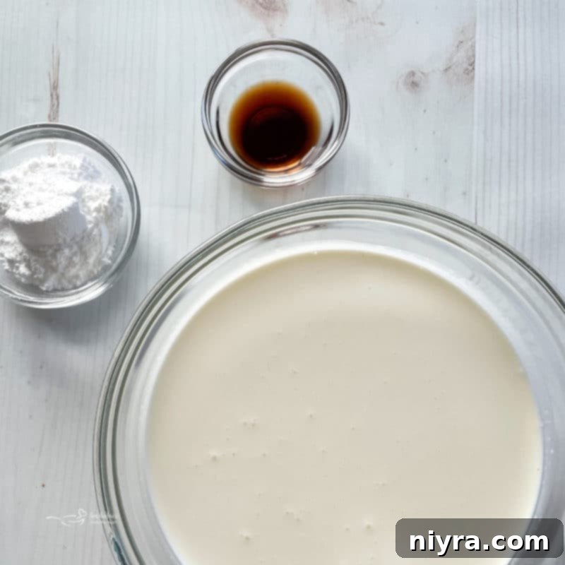 Top view of heavy cream in a bowl, alongside bowls of granulated sugar and vanilla extract, ingredients for whipped topping.
