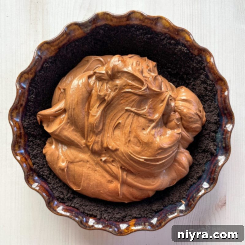 Smooth chocolate filling spread evenly over a prepared chocolate cookie crust in a pie dish.