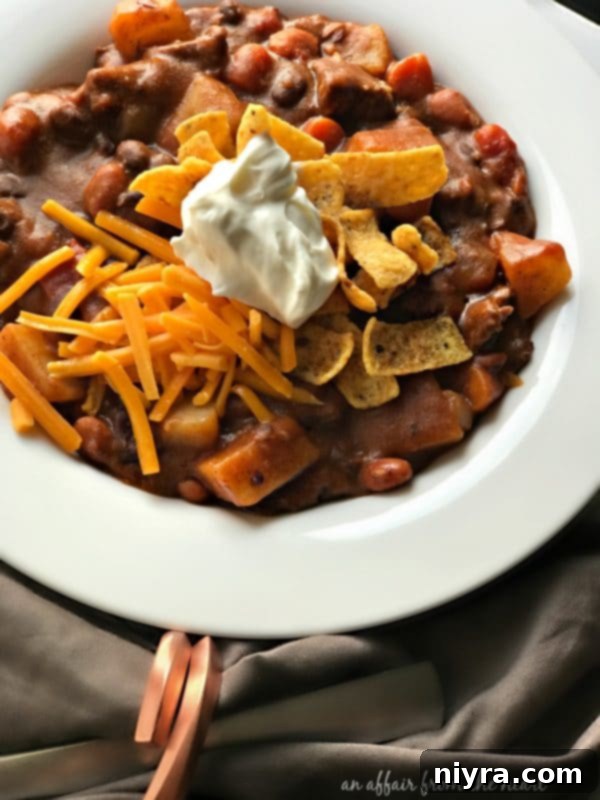 A bowl of Taco Stew topped generously with shredded cheese, sour cream, and corn chips.