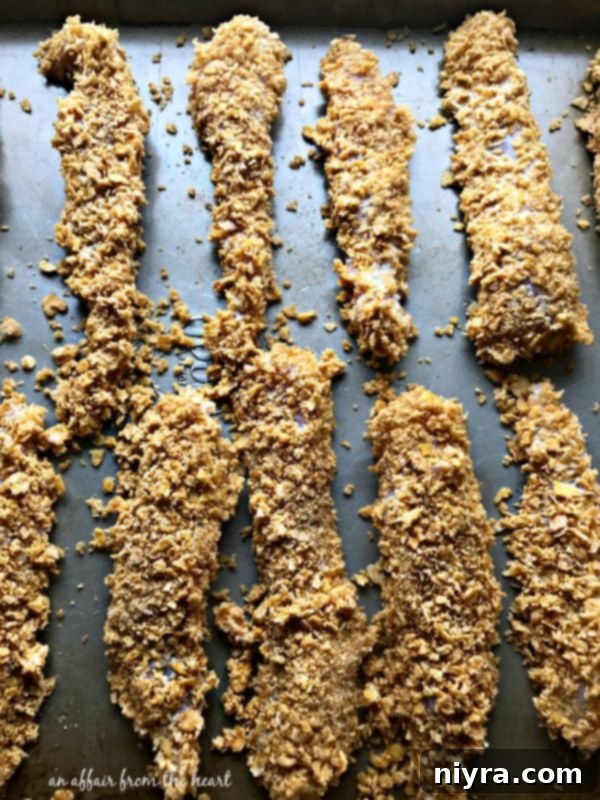 Chicken tender being coated in crushed corn flake cereal and spices