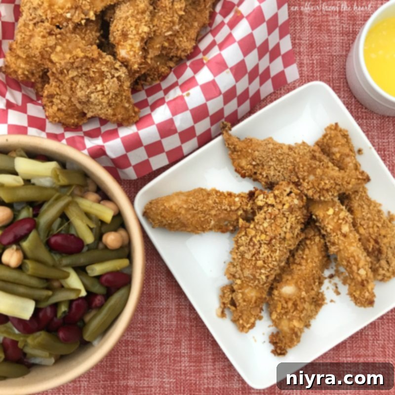 Platter of spicy baked chicken tenders with side dishes including mashed potatoes and a colorful bean salad