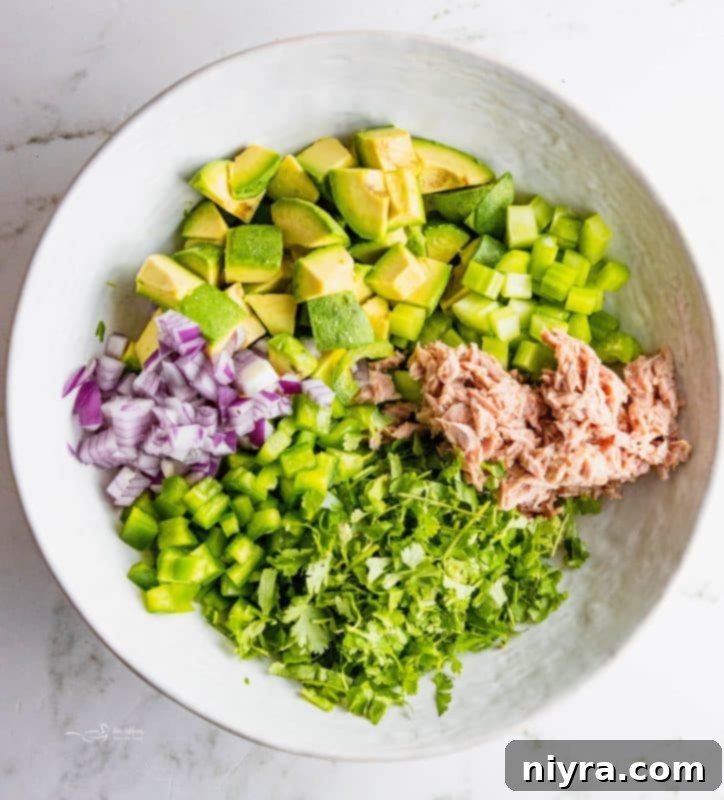 A flat lay of fresh ingredients for avocado tuna salad including avocado, red onion, celery, bell pepper, cilantro, and lemon.