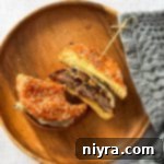 A mushroom Swiss burger cut in half on a wood plate. Half with a bite out of it.