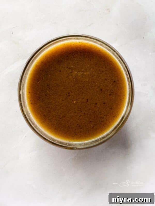 A serving of homemade au jus in a small pitcher, surrounded by ingredients.