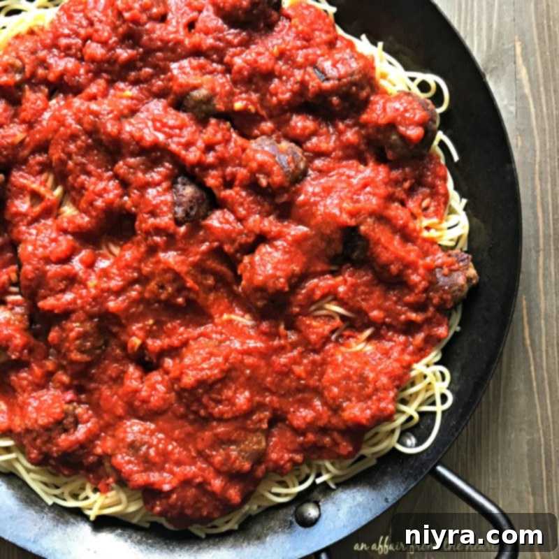 Marinara sauce poured over spaghetti and meatballs