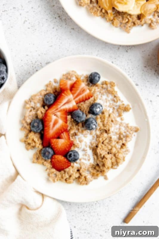 Two bowls of Instant Pot Cinnamon Oatmeal, garnished with fresh berries and banana slices, with a spoon in one bowl.