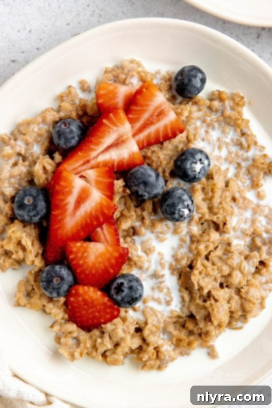 A bowl of Instant Pot Cinnamon Oatmeal with a spoon, decorated with berries and a cinnamon stick.