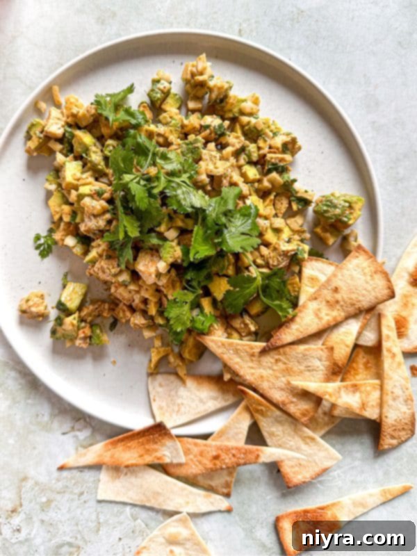 Overhead shot of Avocado Chicken Salad Dip in a white bowl, surrounded by fresh ingredients like avocado, lime, and cilantro.