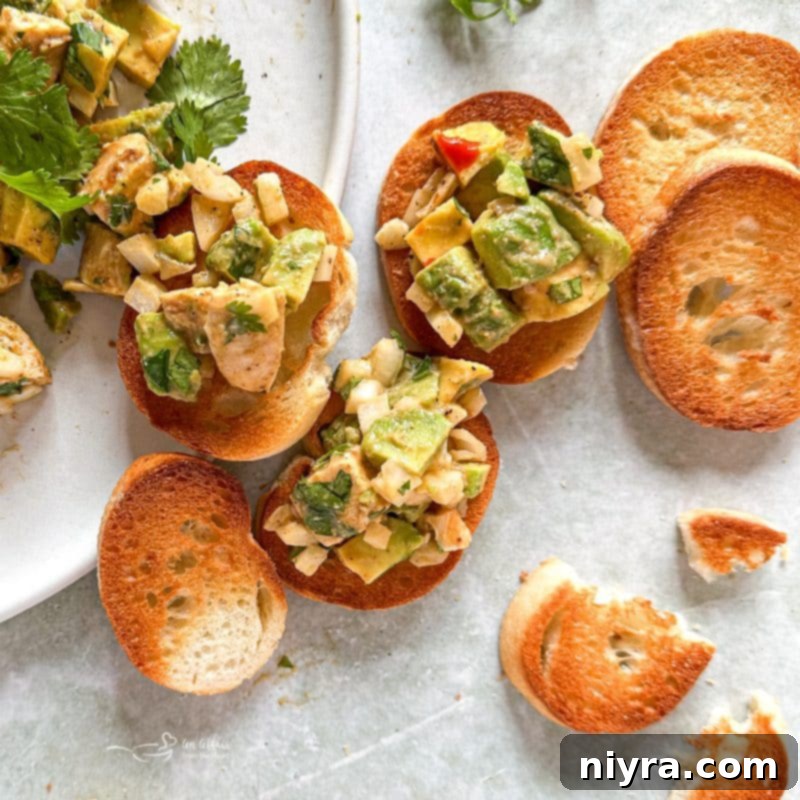 Ingredients for Avocado Chicken Salad Dip laid out on a white surface: diced avocado, cooked chicken, chopped onion, cilantro, sour cream, lemon, and spices.