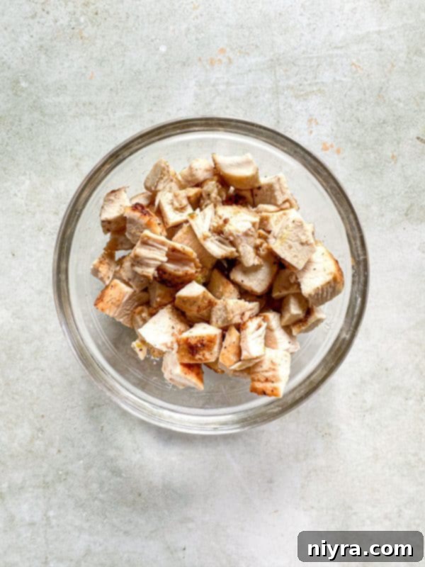 First step in making the dip: cooked chicken breast being diced on a cutting board.