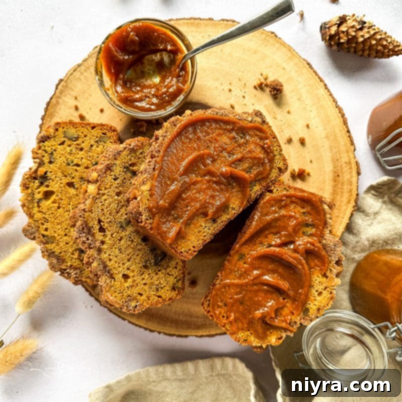 A jar of pumpkin butter beautifully presented next to a slice of pumpkin zucchini streusel bread.