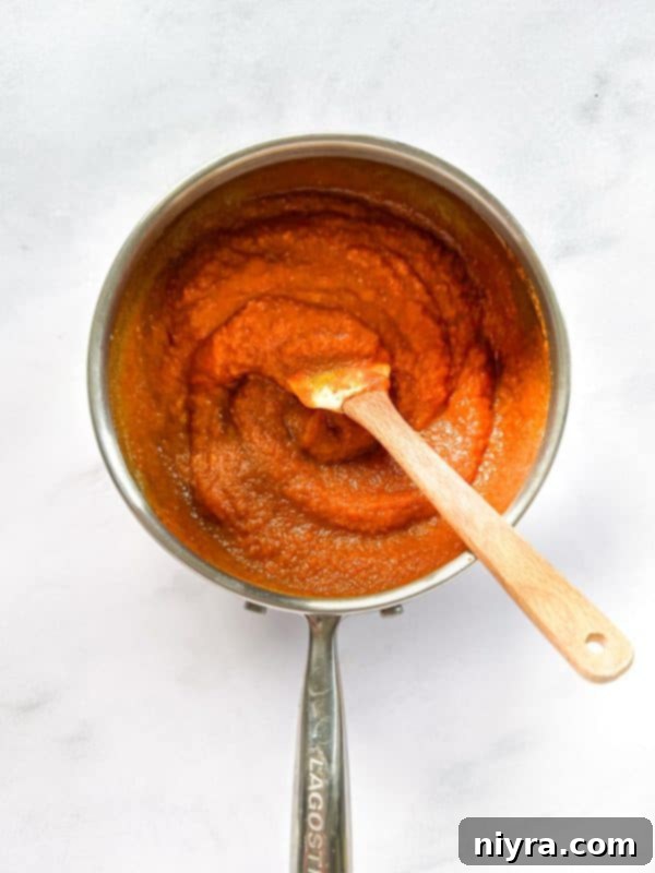 Pumpkin butter simmering in a saucepan on the stove, being stirred.
