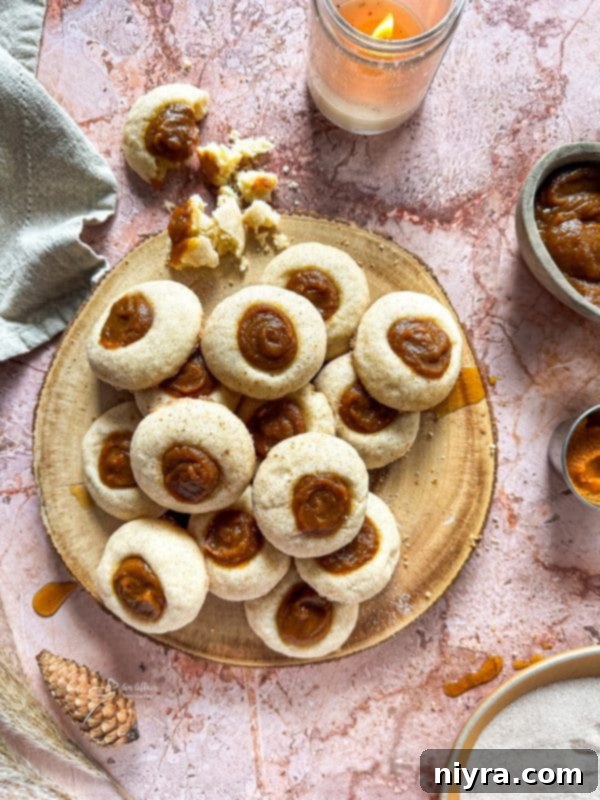 A close-up of a Snickerdoodle Thumbprint Cookie, showcasing its cinnamon-sugar coating and a generous dollop of pumpkin butter.