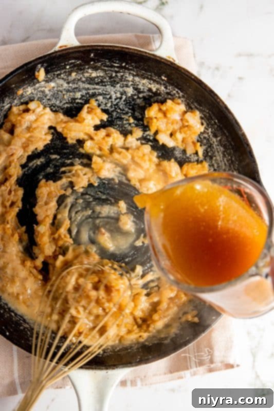 Chicken stock being whisked into the roux in a skillet.