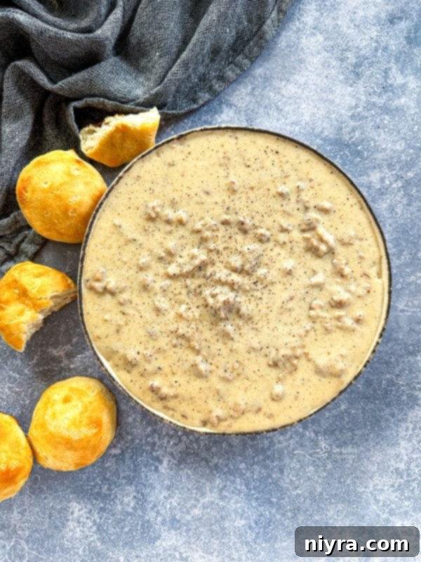 A close-up view of sausage gravy being served with a ladle, showing its thick and inviting consistency.