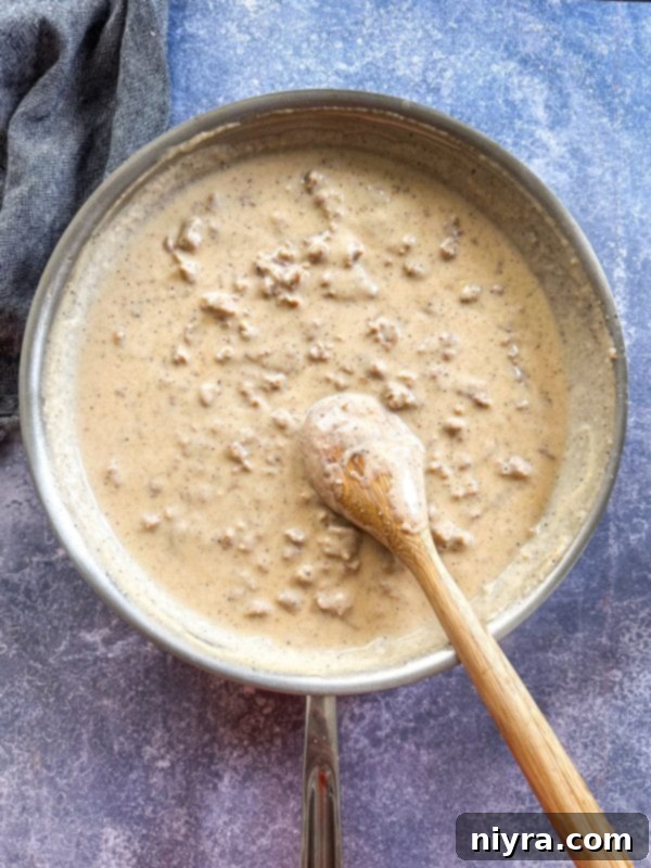Milk being whisked into sausage and flour mixture for gravy, illustrating the technique for a smooth consistency.