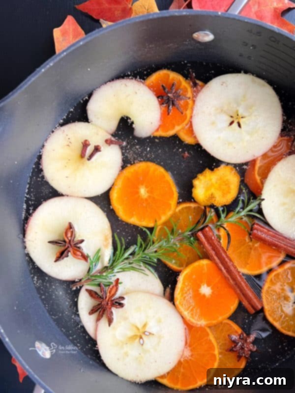 A beautifully arranged autumn simmer pot with sliced oranges, apples, cinnamon sticks, and star anise in a pot on a stovetop, ready to simmer.