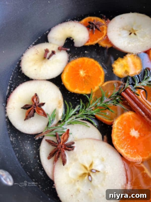 A glass pot filled with autumn simmer pot ingredients, sitting on a wooden surface with diffused light.
