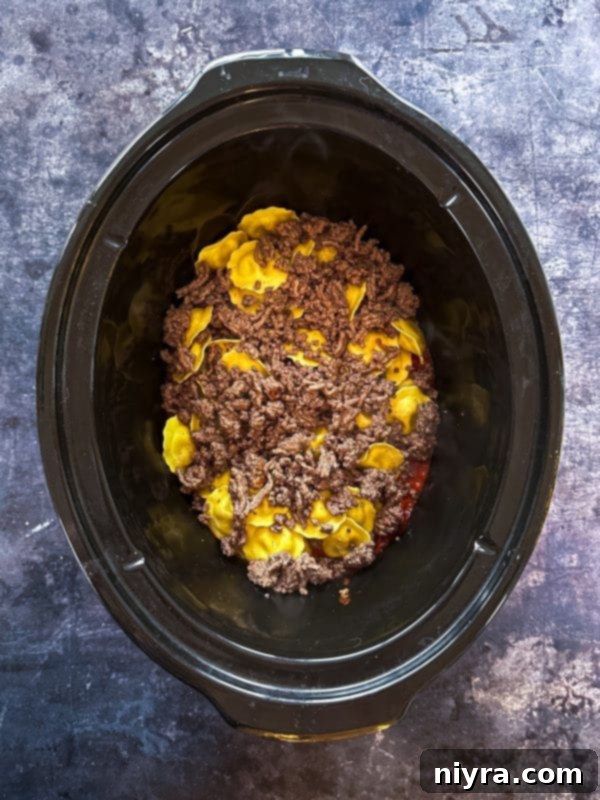 Step 4: Layering half of the frozen ravioli over the sauce in the slow cooker.