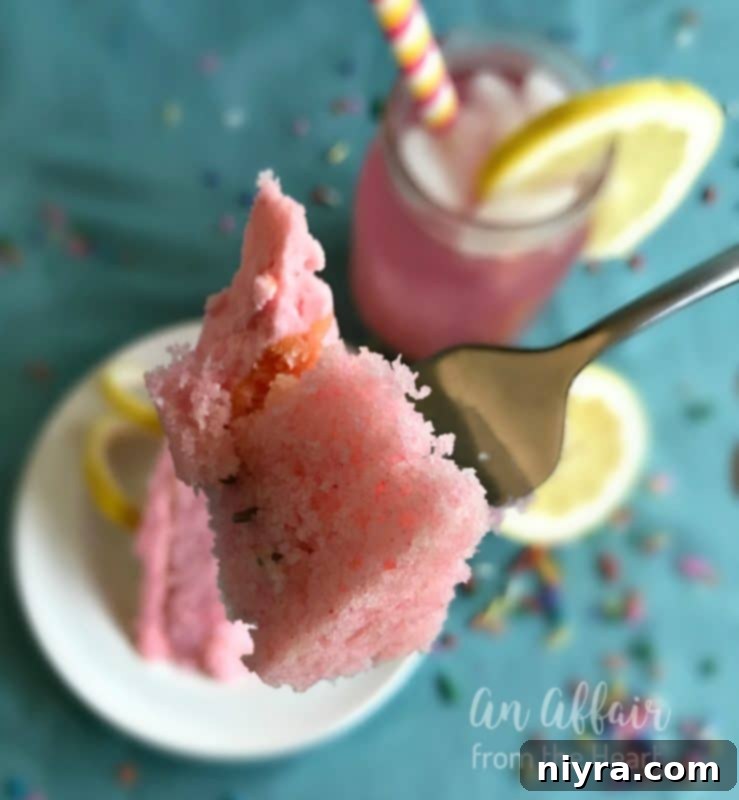A slice of Pink Lemonade Cake on a white plate, showing the moist cake layers and smooth pink frosting, garnished with a fresh lemon wedge.