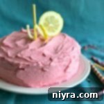 Pink Lemonade Cake slice on a white serving plate, showing moist cake and creamy frosting.