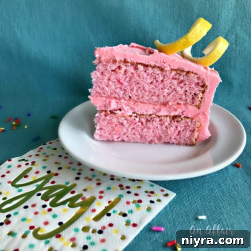 A beautifully decorated Pink Lemonade Cake on a rustic wooden stand, surrounded by fresh lemons and pink flowers, ideal for a spring or summer party.