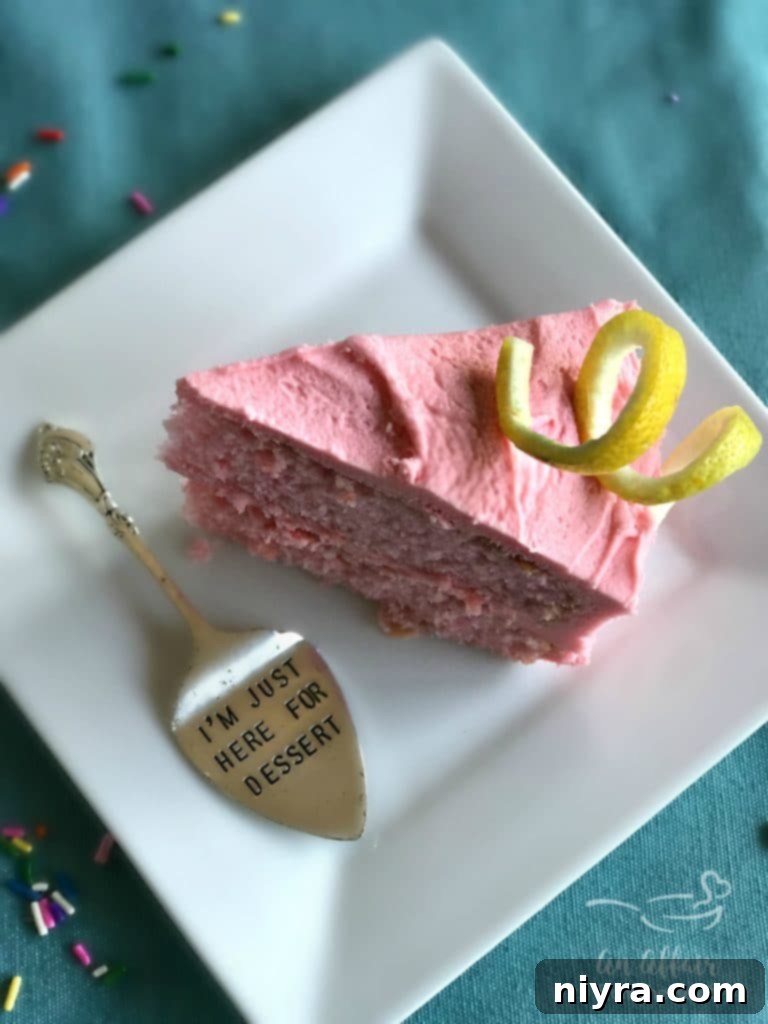 Close-up of a Pink Lemonade Cake slice, perfectly moist and fluffy, with a generous swirl of pink frosting, highlighting the beautiful layers.