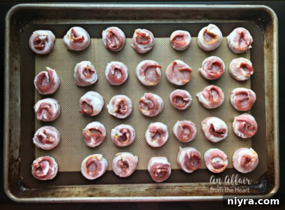 Bacon-wrapped sausage bites arranged on a baking sheet lined with a Silpat mat.
