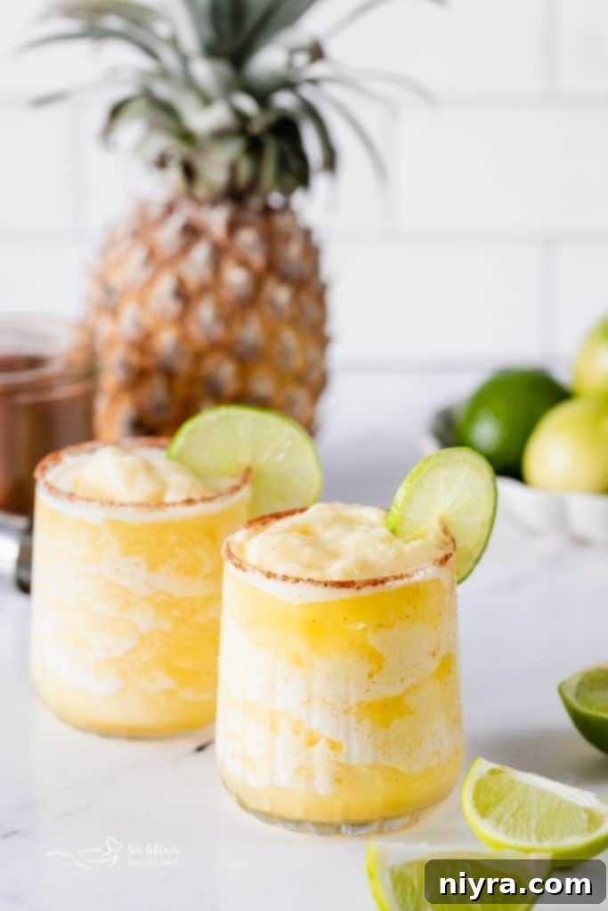 A close-up shot of a single Frozen Pineapple Margarita, adorned with a fresh lime wedge, against a soft, sunlit background.