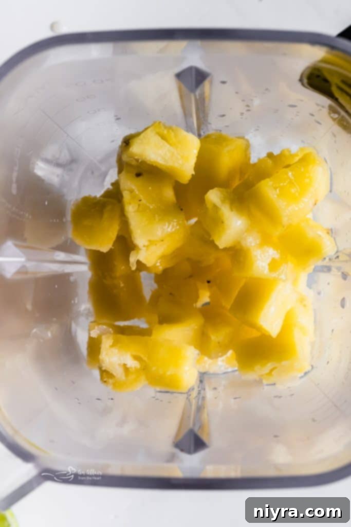 Fresh pineapple chunks, lime, and jalapeño being added to a blender for a frozen margarita.