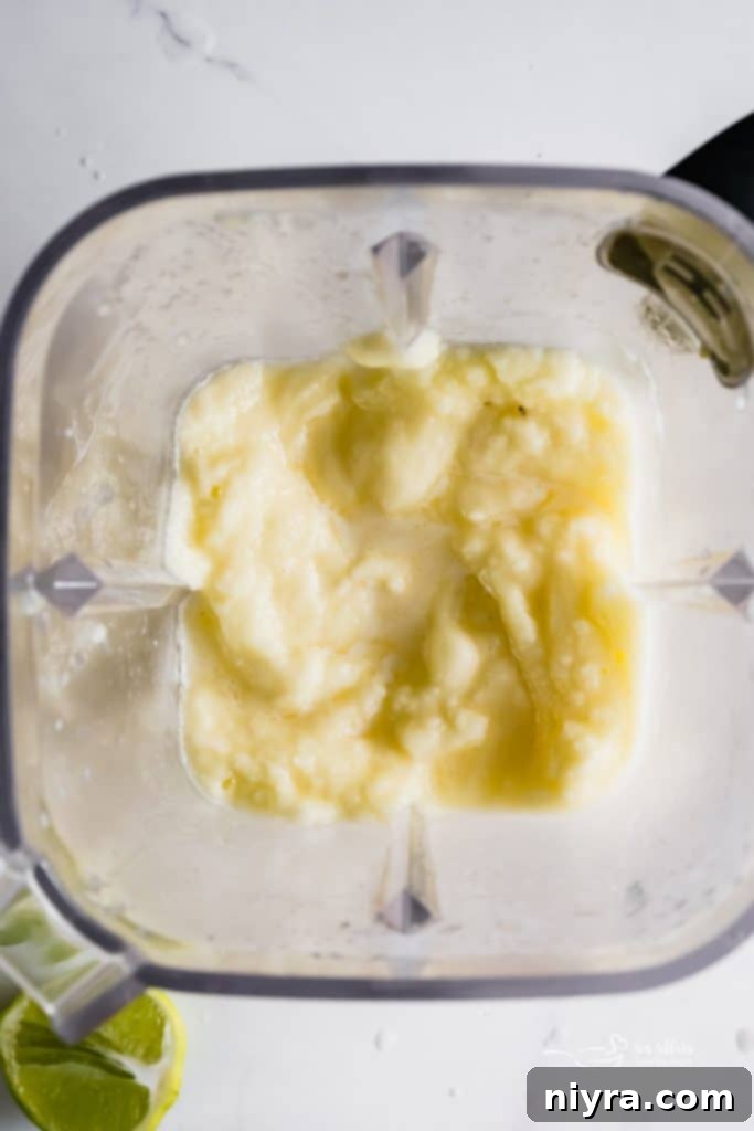 A blender filled with a smooth, bright yellow frozen pineapple margarita mixture, ready to be poured.