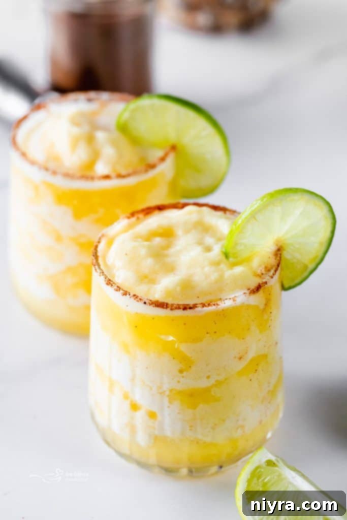An overhead view of two Frozen Pineapple Margaritas, accompanied by a pitcher and fresh pineapple slices, ready for a party.