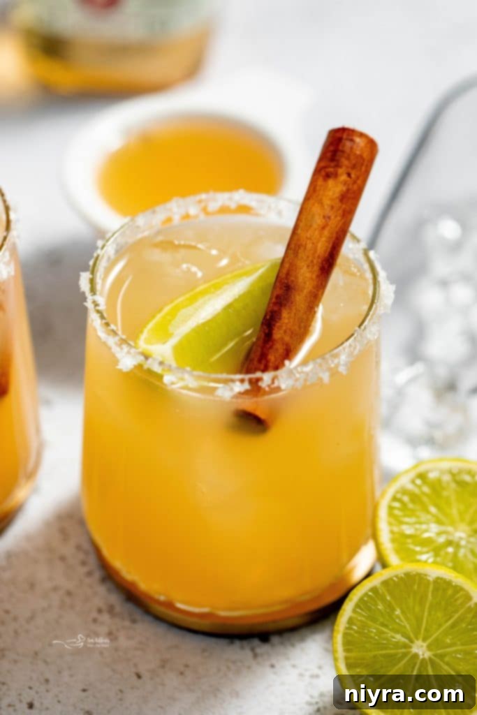 Close up of an Apple Cider Margarita in a glass with a sugar rim and apple slices, served on a wooden board, tempting fall flavors.