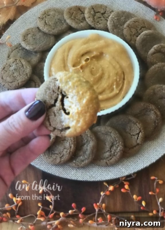 A hand holding a spice cookie, poised to dip into the creamy pumpkin dip, inviting the reader to try.