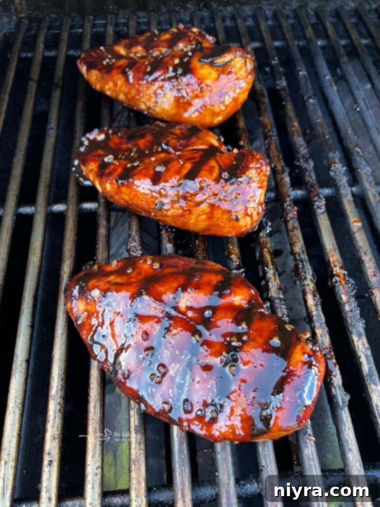 Cooked chicken breasts on the grill being basted with the heated sweet and smoky marinade.
