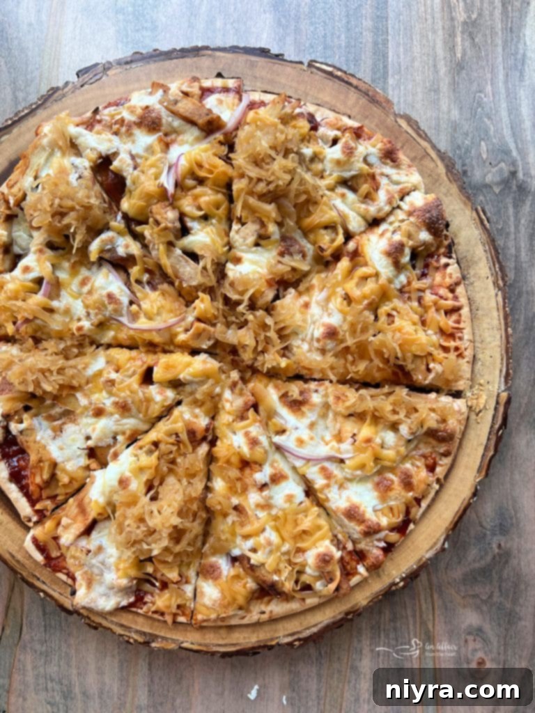 Overhead shot of a slice of BBQ Chicken Pizza with kraut and a full pizza in the background.