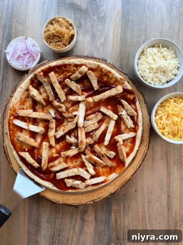 Layering grilled chicken and red onion on the pizza crust.