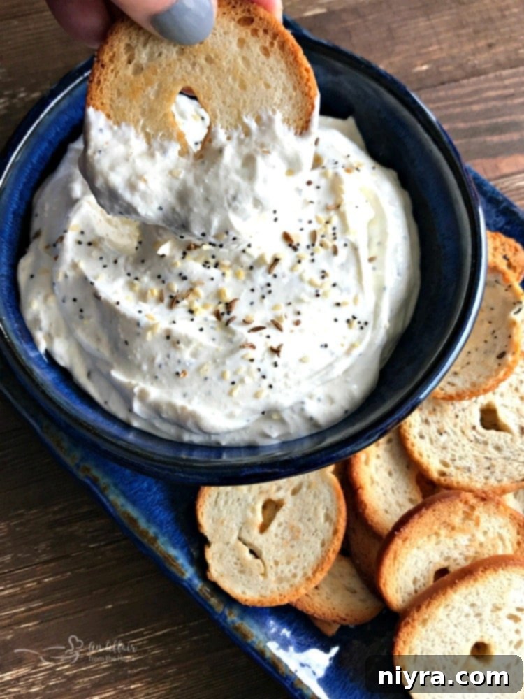 Everything Bagel Dip in a blue bowl with a bagel chip for dipping.