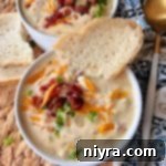 Close up of a bowl of Creamy Bacon soup topped with a piece of bread on the side of the bowl.