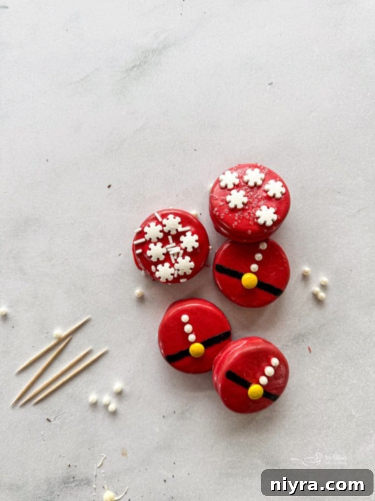 Close-up of Santa Suit Oreos on a white plate, showcasing the red chocolate coating, black belt, yellow buckle, and white sugar pearl buttons.