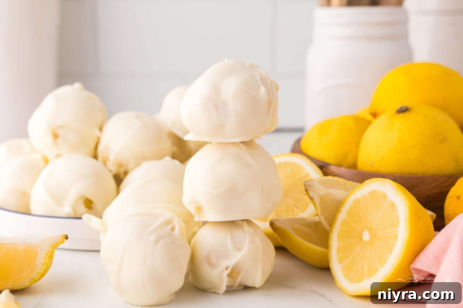 Stacked lemon truffles next to fresh lemons, highlighting the main ingredient.