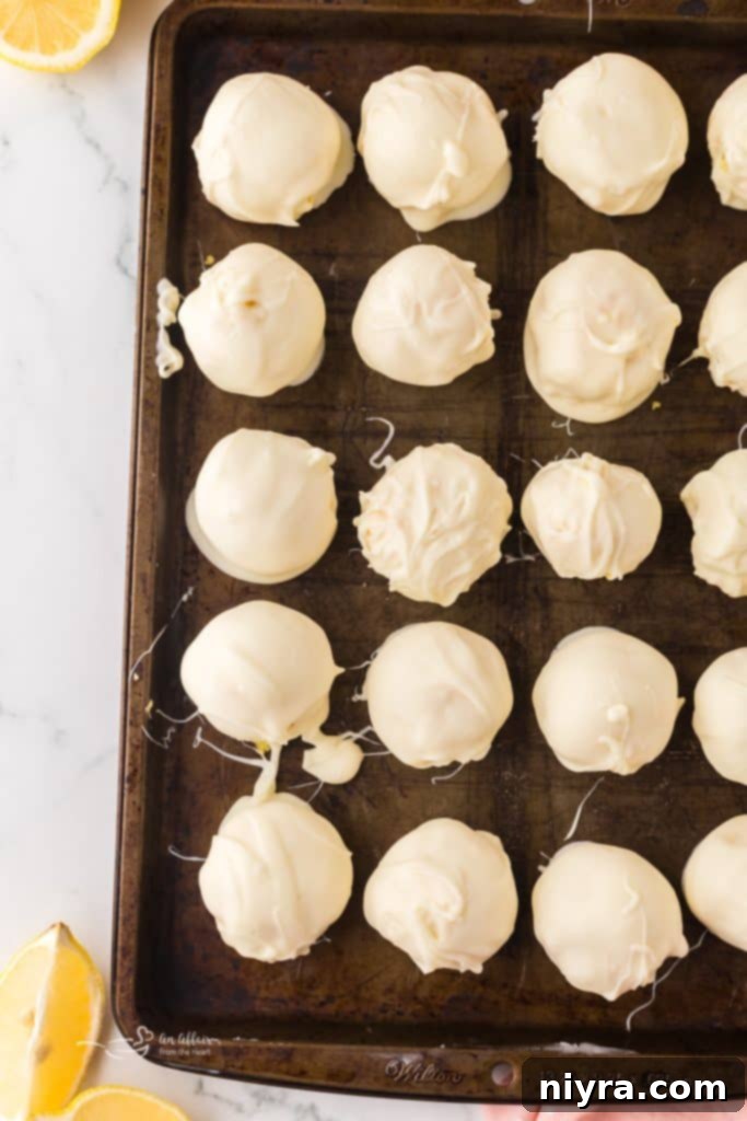 A lemon truffle being dipped into a bowl of melted white chocolate, with lemon zest mixed in.