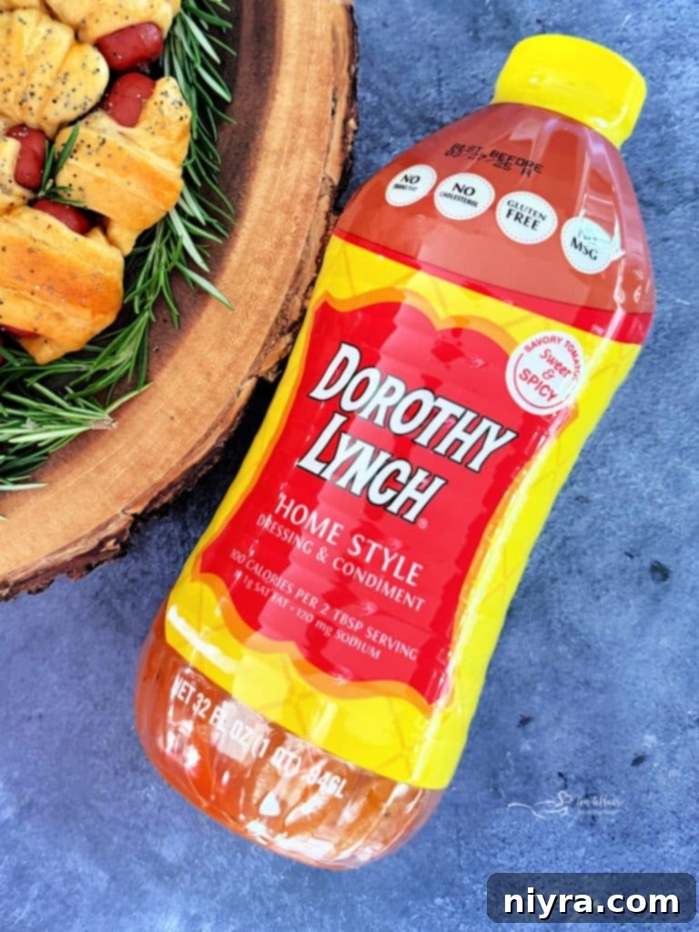 Pigs in a Blanket Wreath with a dipping bowl of Dorothy Lynch, fresh rosemary, and scattered poppy seeds.