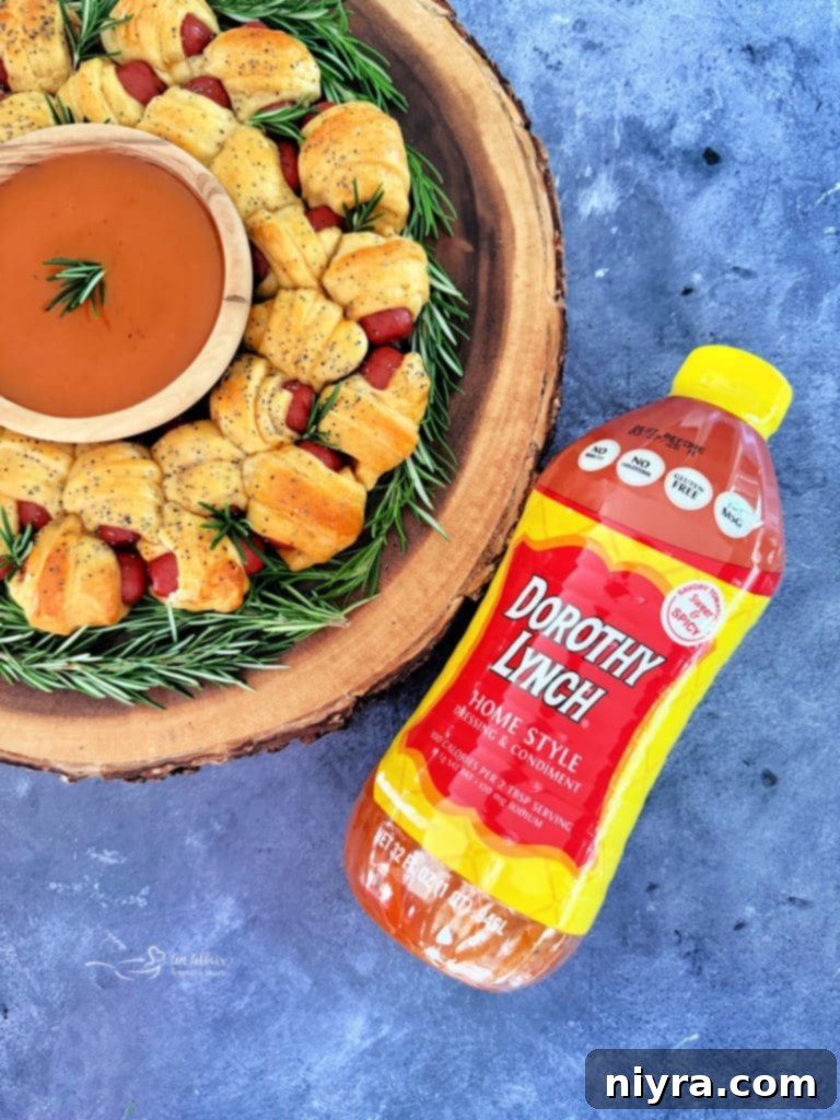 Close-up of a golden brown Pigs in a Blanket Wreath garnished with fresh rosemary, ready to be served with a dip.