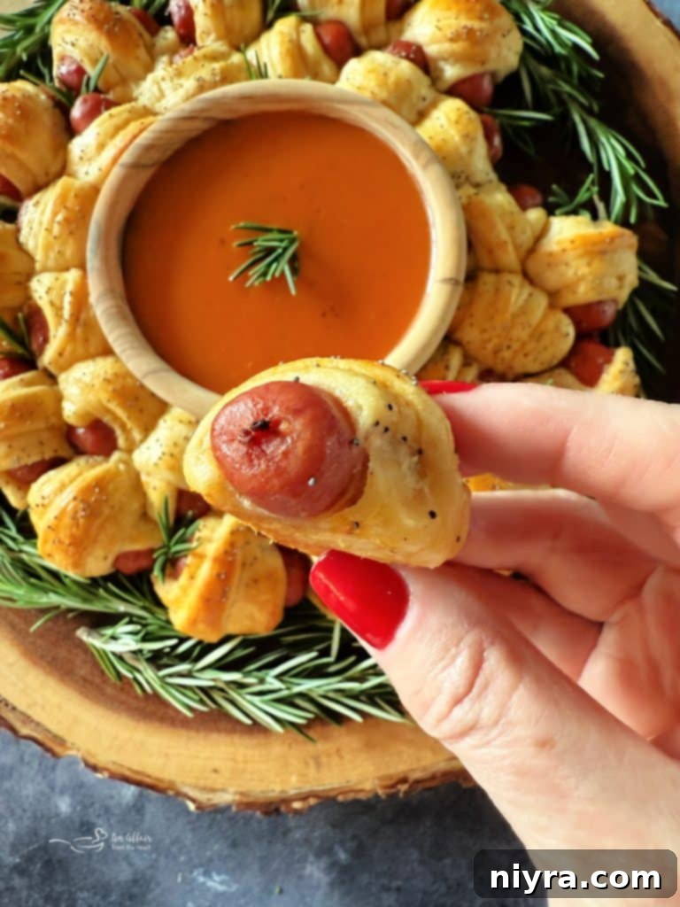 Golden Pigs in a Blanket Wreath on a wooden serving board, garnished with fresh herbs, ready for a festive party.