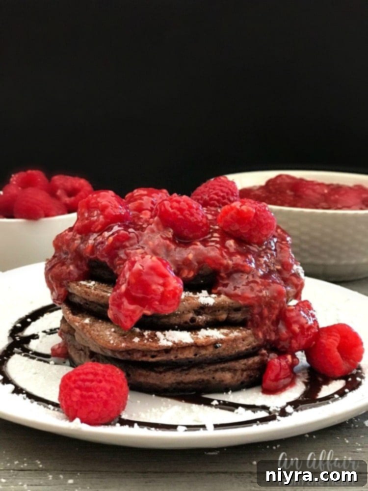 Fluffy chocolate pancakes drizzled with homemade raspberry sauce and powdered sugar