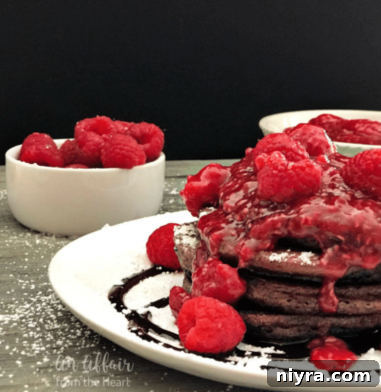 Stack of fluffy chocolate pancakes with raspberry sauce and powdered sugar