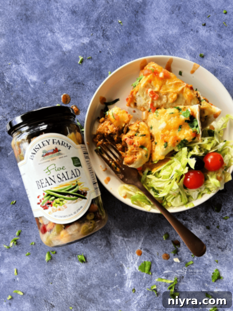 Enchiladas and a side salad on a plate next to a jar of Paisley Farm five bean salad.