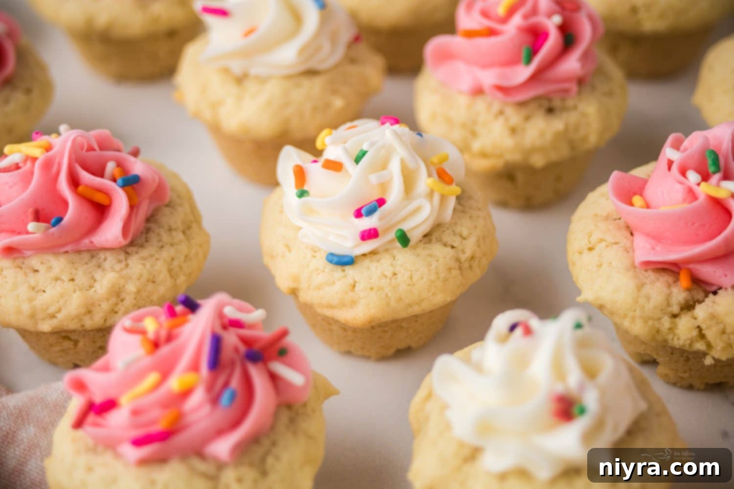 Frosted Sugar Cookie Delights 3 A tray of freshly baked sugar cookie cups, some frosted with pink and white frosting and sprinkles.