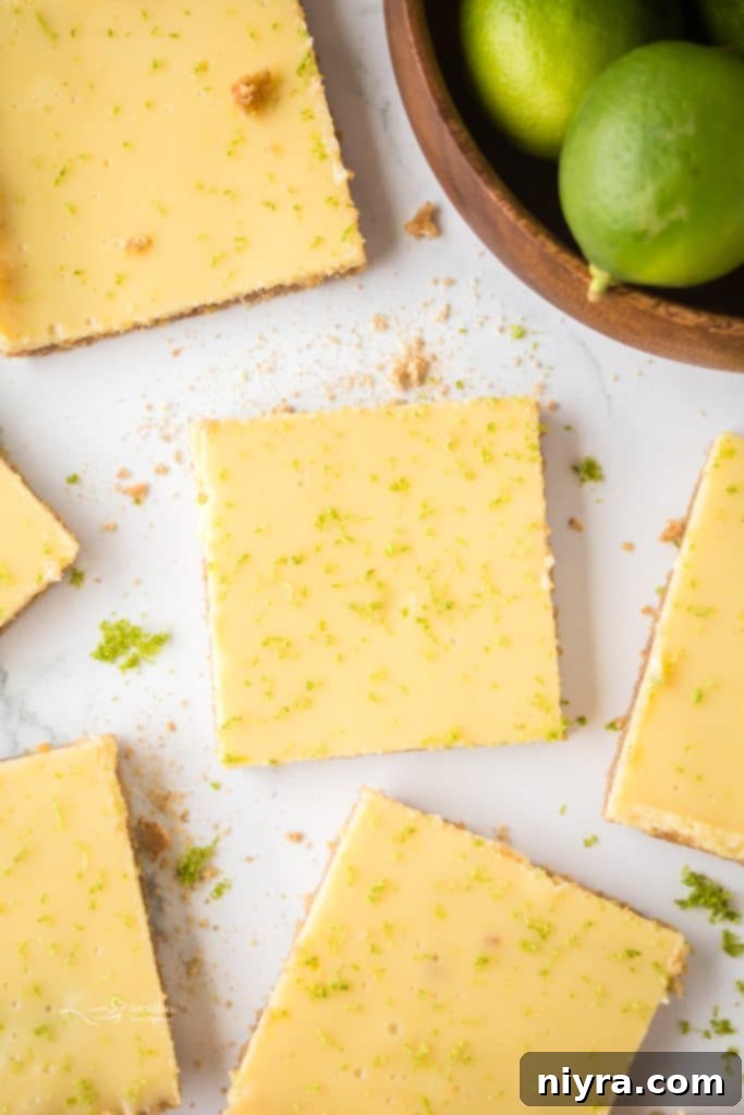 Zesty Key Lime Pie Bars 2 Close-up of a square Key Lime Pie Bar with a golden crust and pale green filling, garnished with fresh lime zest.